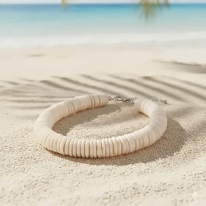 Tropical puka shell necklace resting on white sand, evoking a relaxed, Hawaiian beach vacation aesthetic.