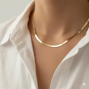 A photo of a flat, liquid-like herringbone gold chain necklace, a popular and elegant style that rests smoothly against the collarbone.