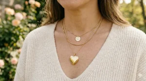 A photorealistic 4K detailed photograph of a woman wearing a layered jewelry look, featuring a personalized gold heart-shaped photo locket necklace styled with other delicate gold chains.