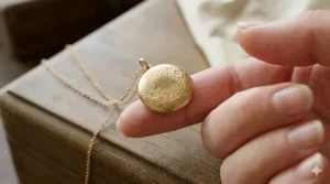 A small gold locket necklace dainty pendant held between fingers to demonstrate its petite scale and delicate craftsmanship.